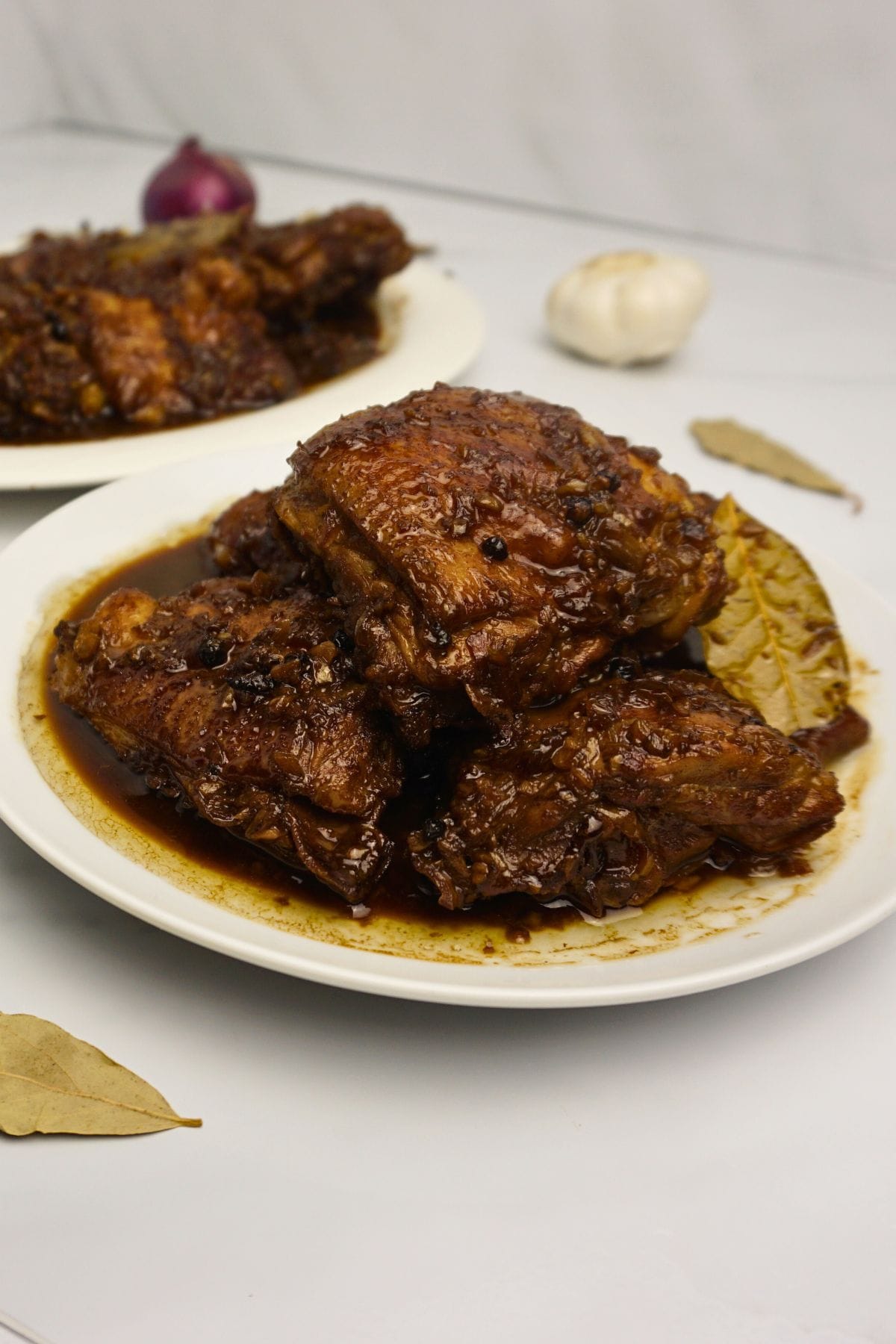 Plates of chicken adobo with fresh garlic and laurel leaves on the background.