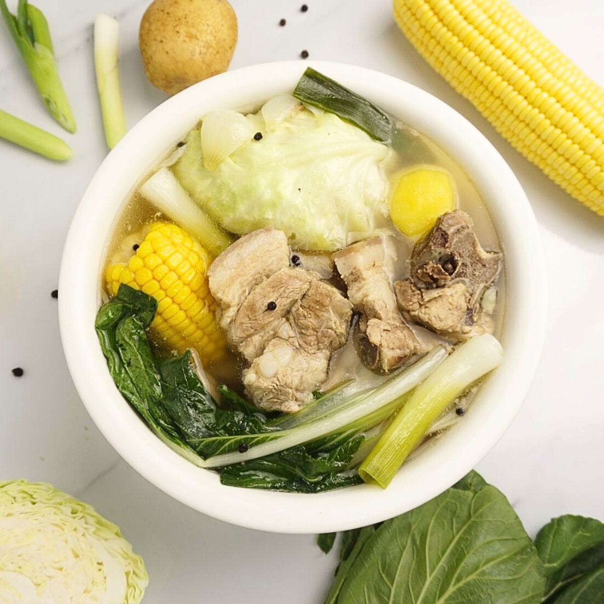 Pork nilaga in bowl with raw ingredients on the side.