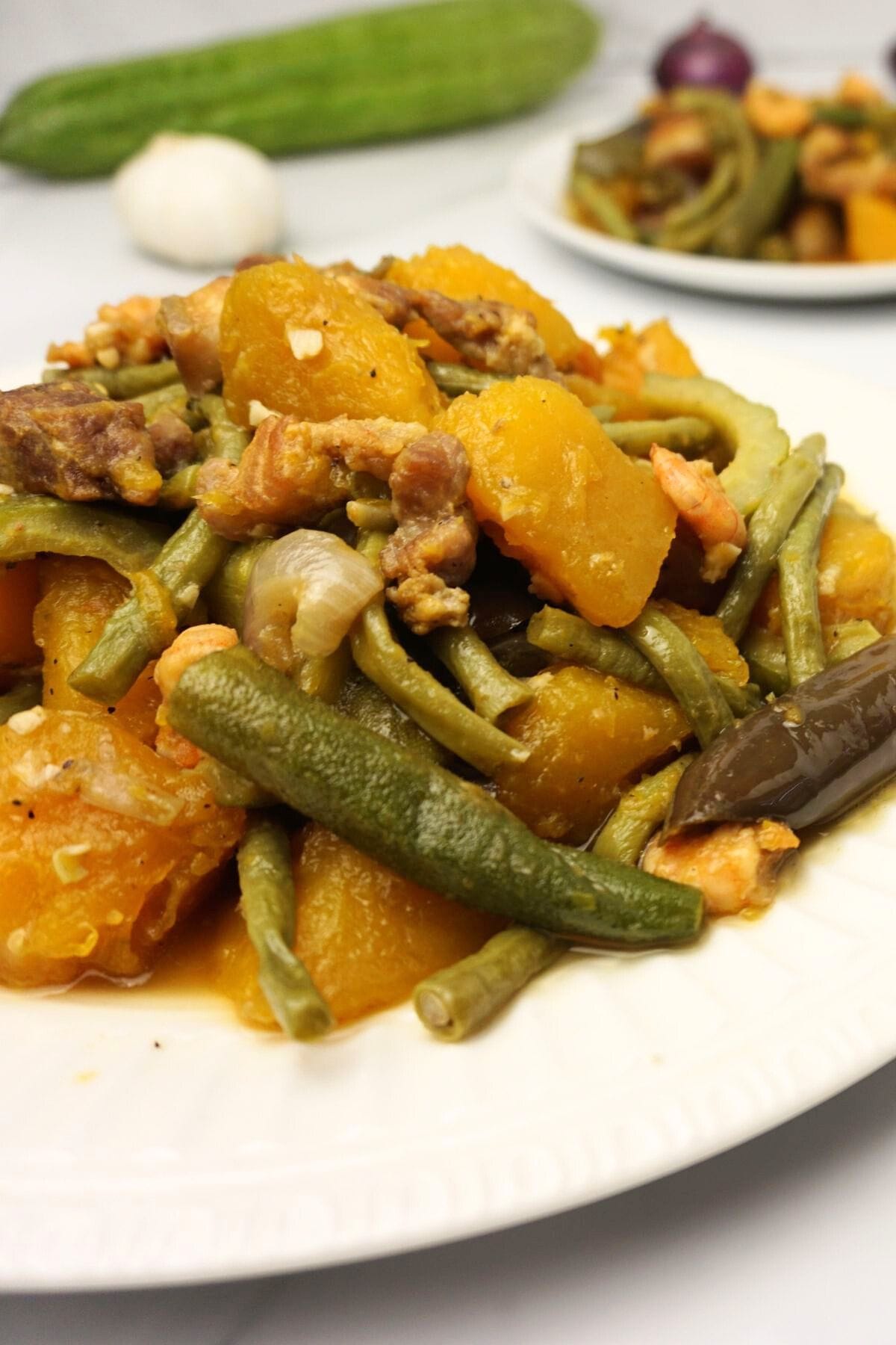 Platers of pinakbet on a white marble table with garlic and bitter gourd on the background.