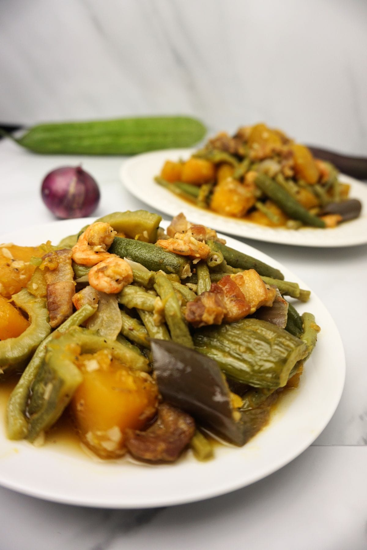 Two servings of pinakbet on a white marble table.