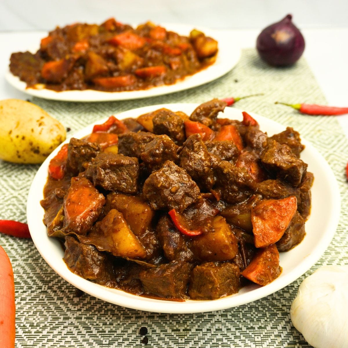 Spicy beef caldereta serve on plates with fresh ingredients on the side.
