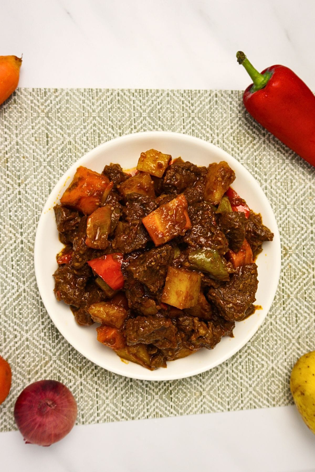Top view of a plater of beef mechado with fresh ingredients on the side