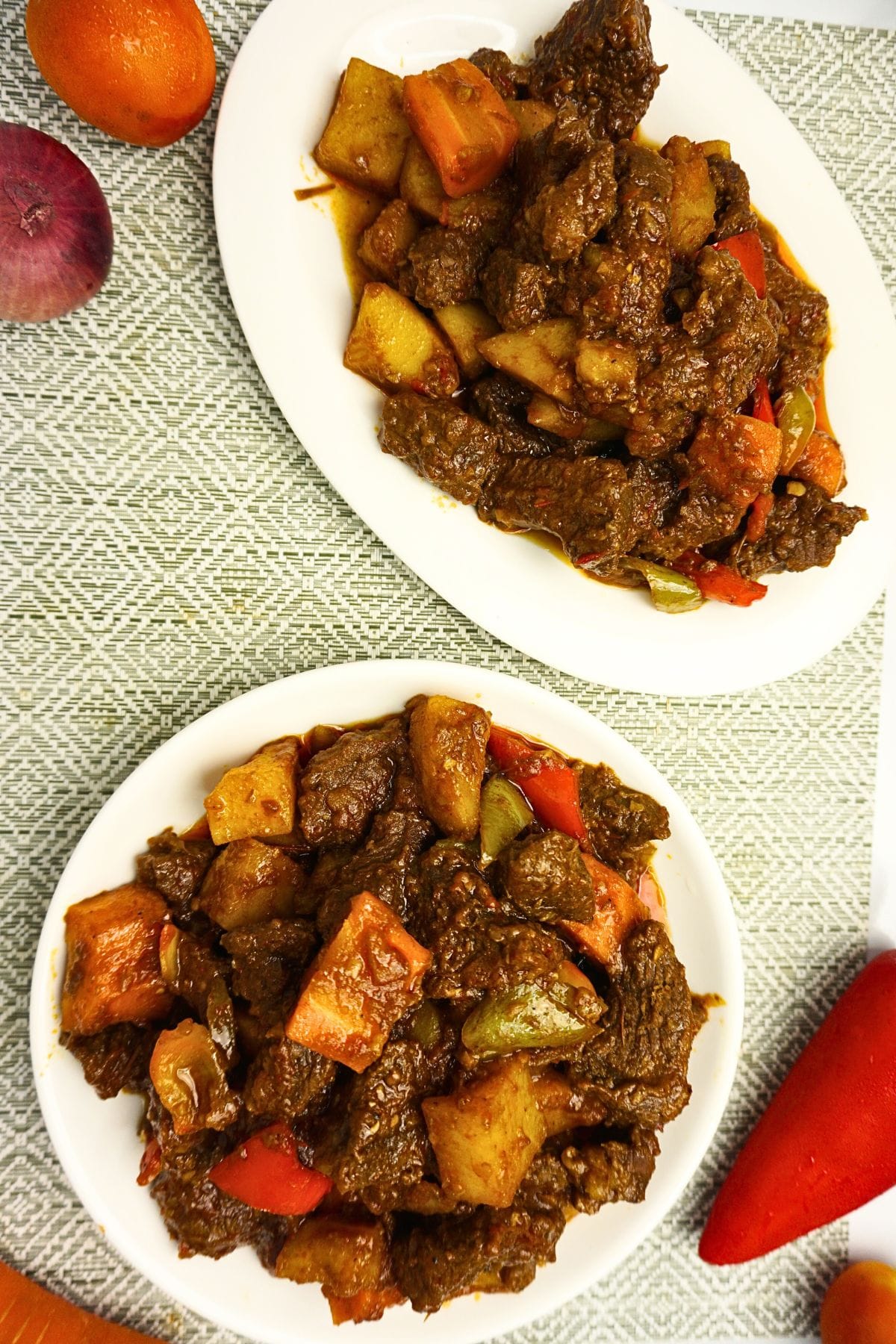 Plater of beef mechado with fresh tomato, onion, carrot and bell pepper on a table.