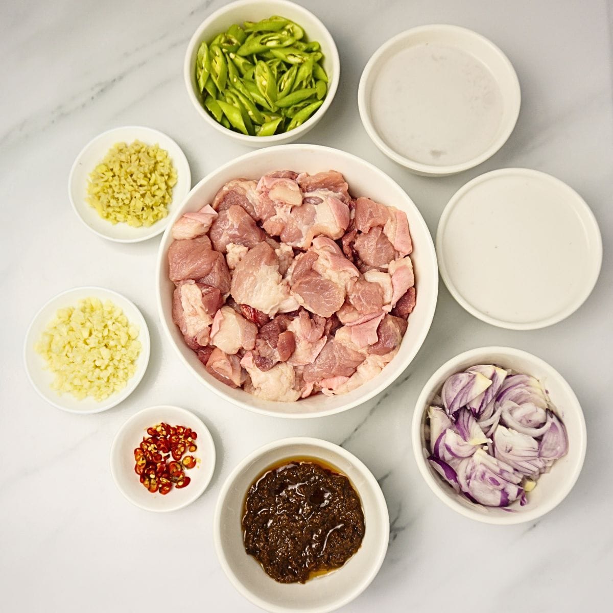 Bowl of pork belly, ginger, garlic, onion. green chilis, red chilis, coconut milk and coconut cream.