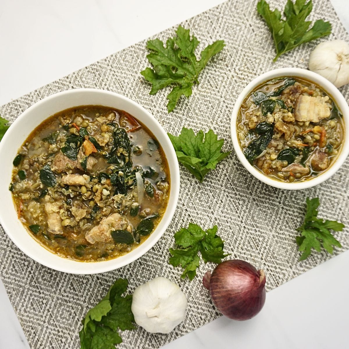 Top view of bowls of ginisang monggo wih onion, garlic and ampalaya leaves on the side.