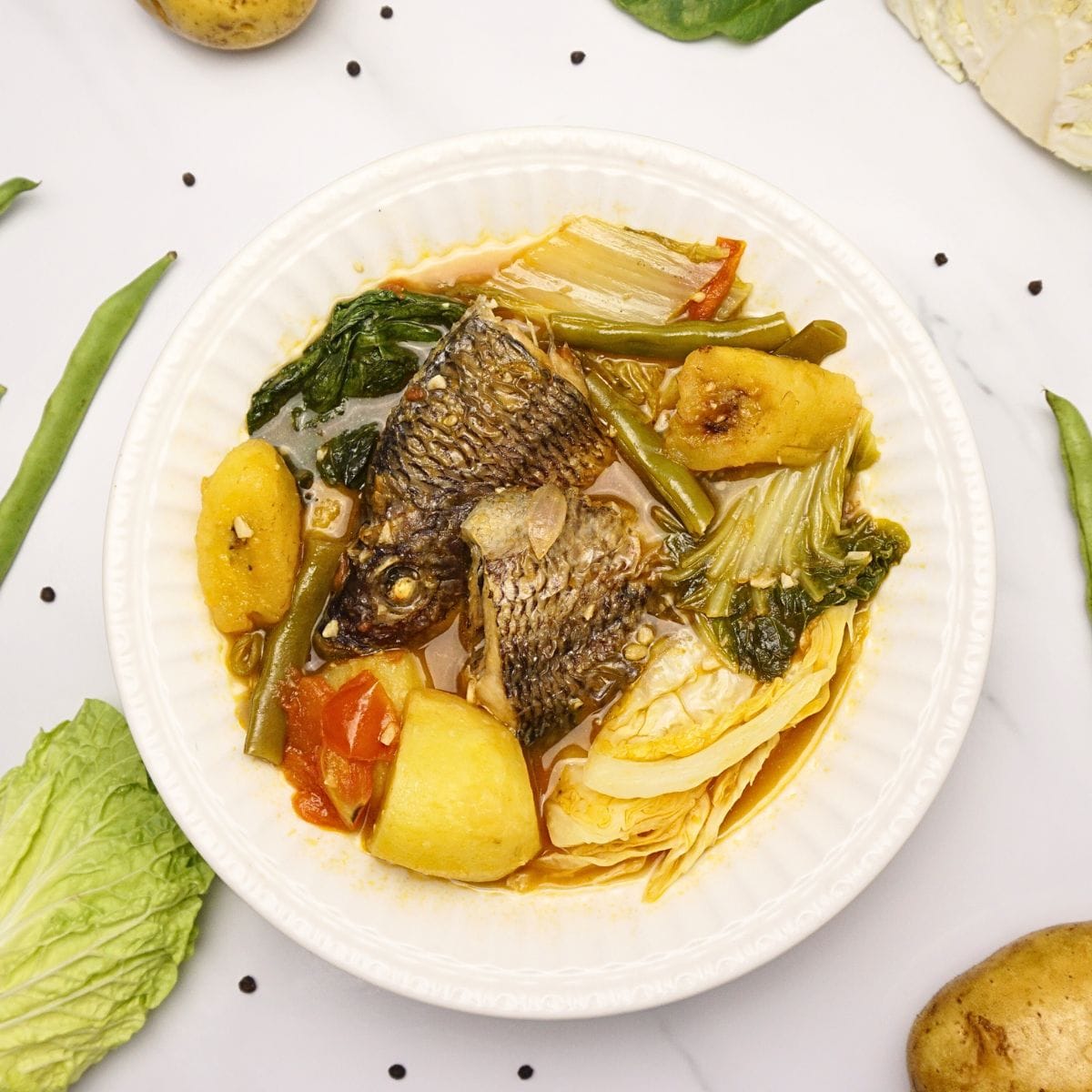 Plater of pocherong tilapia on a marble table with fresh vegetables on the side.
