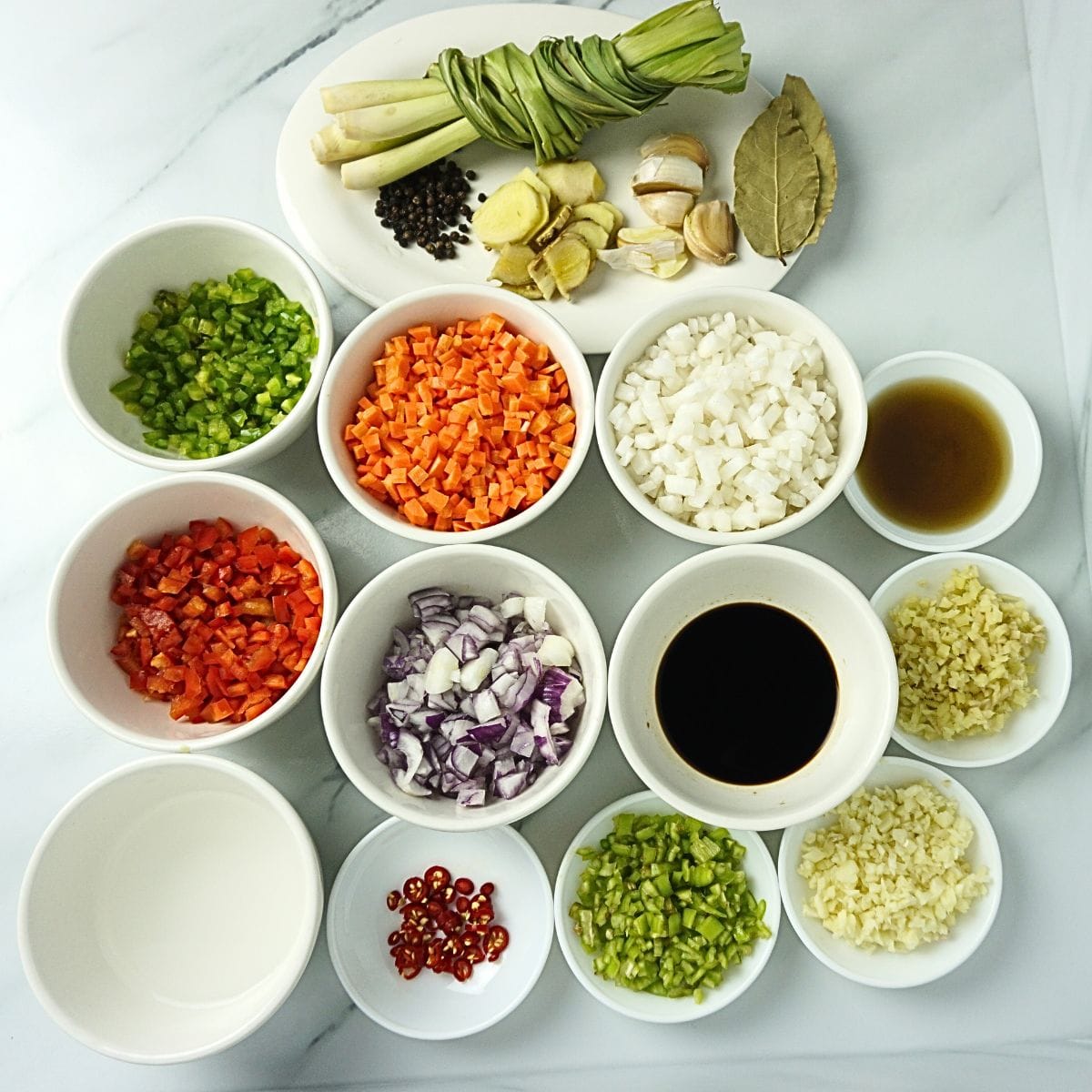 Bowls of bopis ingredients. Vinegar, red chilis. green chilis, garlic, onion, soy sauce, ginger, red bell pepper, green bell pepper, carrots, radish, fish sauce, lemongrass, bay leaves and black pepper.