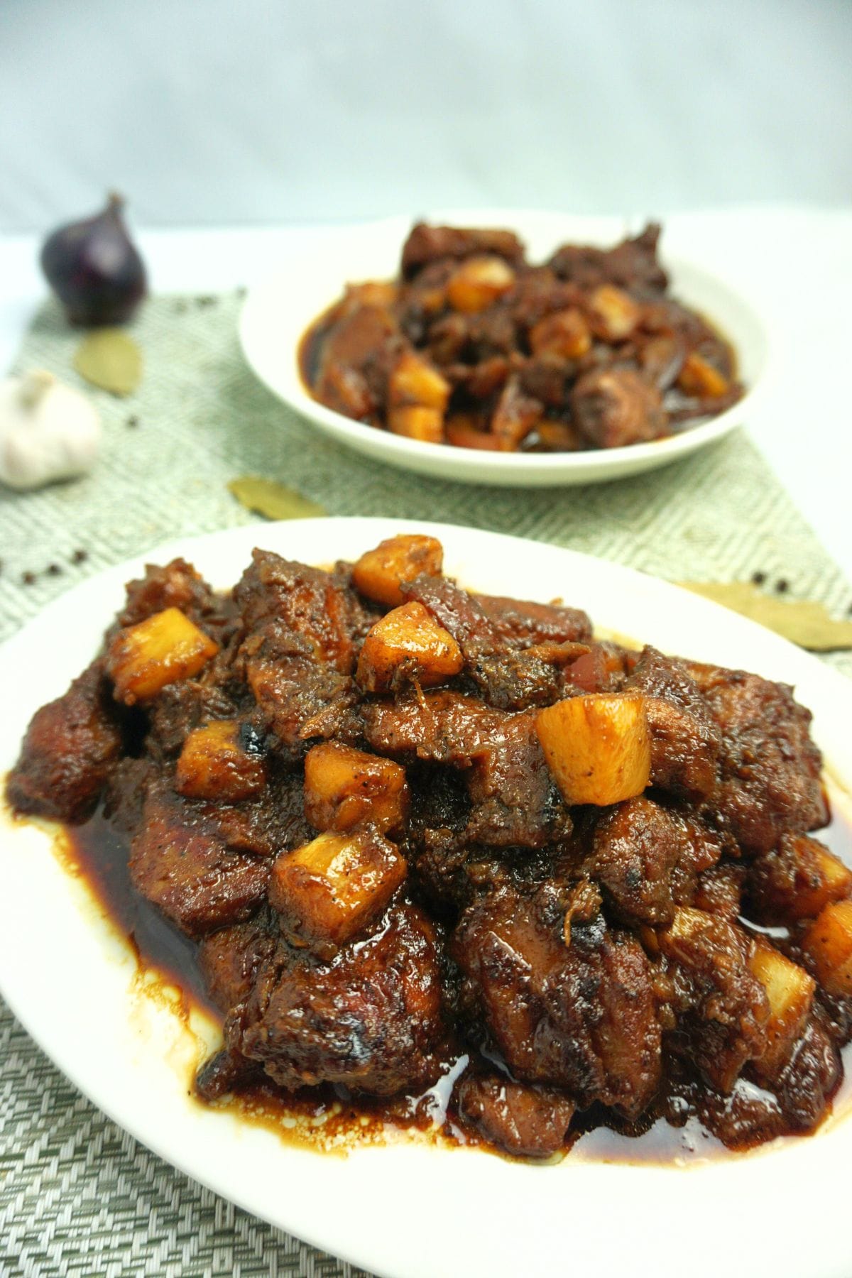 Two plates of pork hamonado with fresh garlic and onion on table.