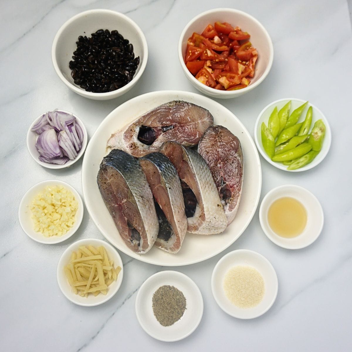 Bangus with tausi ingredients in bowls. Bangus belly, ginger, garlic, onion, tausi, tomatoes, green chilies, fish sauce, black pepper and cooking oil.