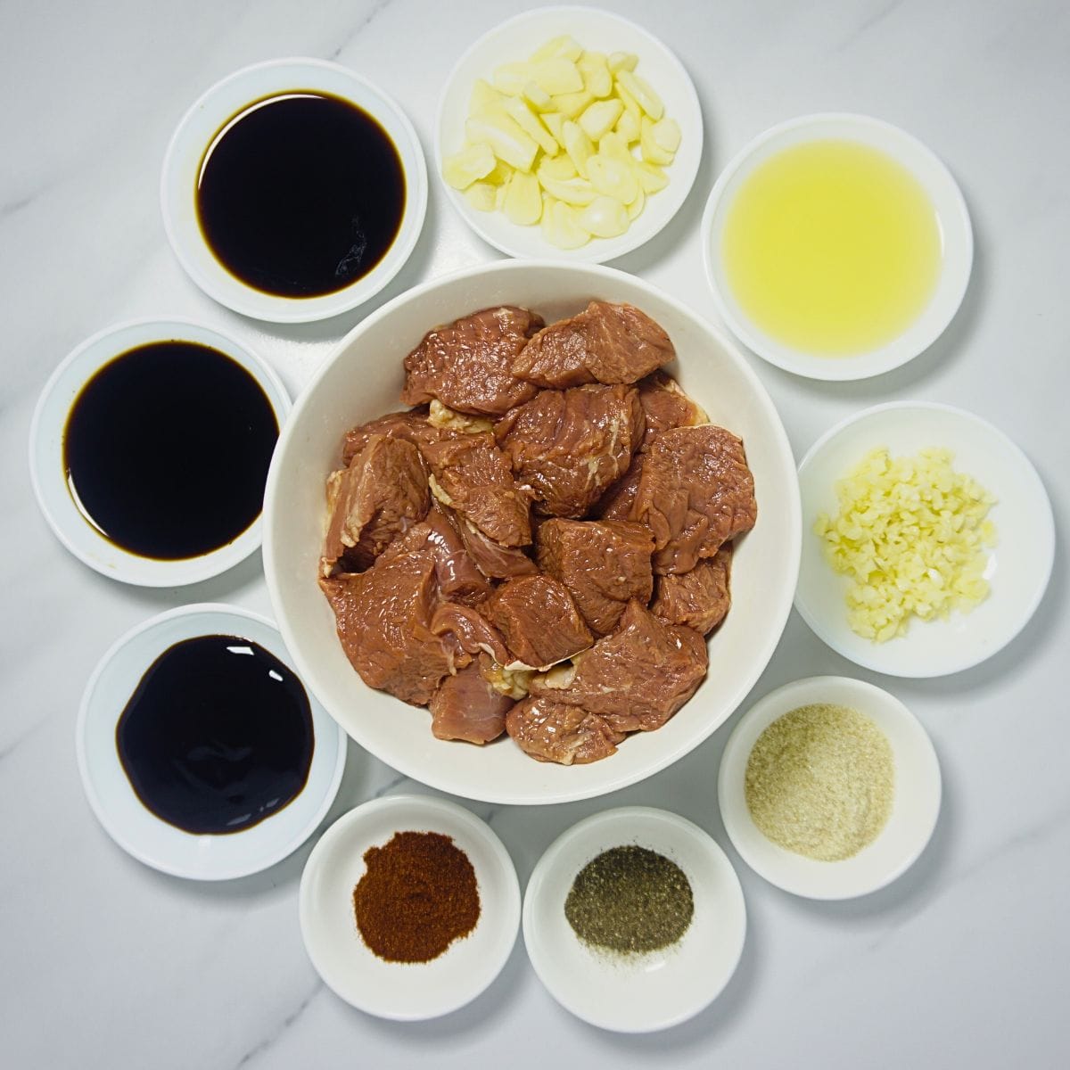 Beef tenderloin, Worcestershire sauce, butter, minced garlic, soy sauce, oyster sauce, black pepper, and a pinch of salt on a marble table.