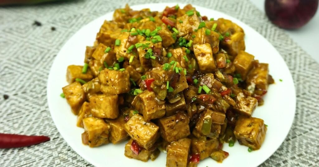 Tofu Sisig in plate garnished chopped green onions.