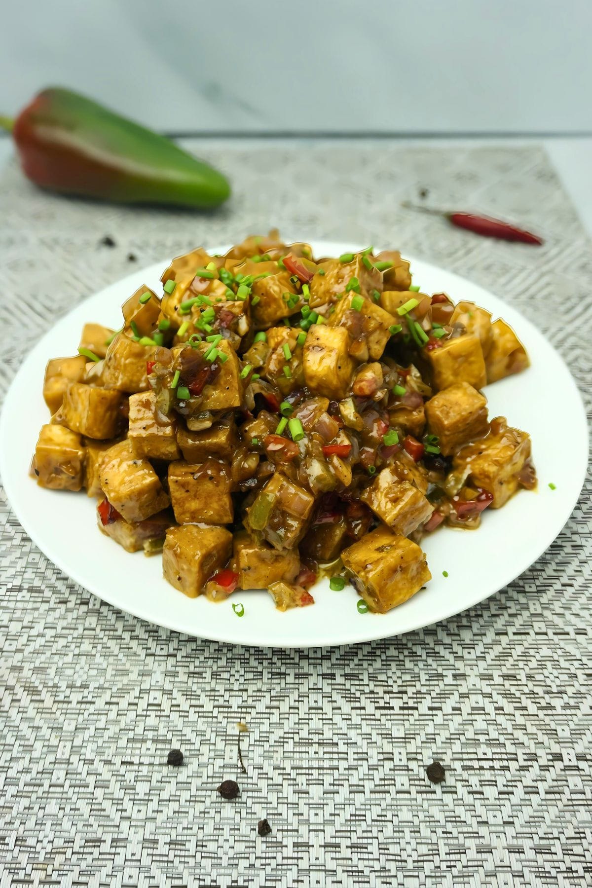 Plate of tofu sisig in a table with fresh chili and bell pepper on the side,