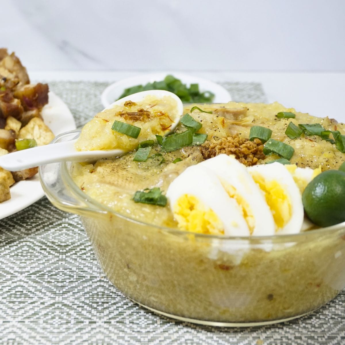Bowl of arroz caldo with sliced boiled egg, green onions, fried garlic and calamansi on top.