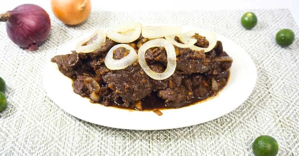 Plate of bistek tagalog with fresh calamansi and onions on a table.