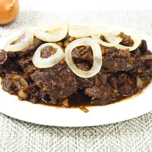 Plate of bistek tagalog with fresh calamansi and onions on a table.