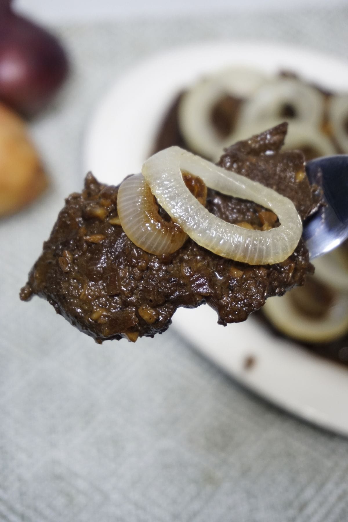 Spoon scooping a portion of bistek tagalog.