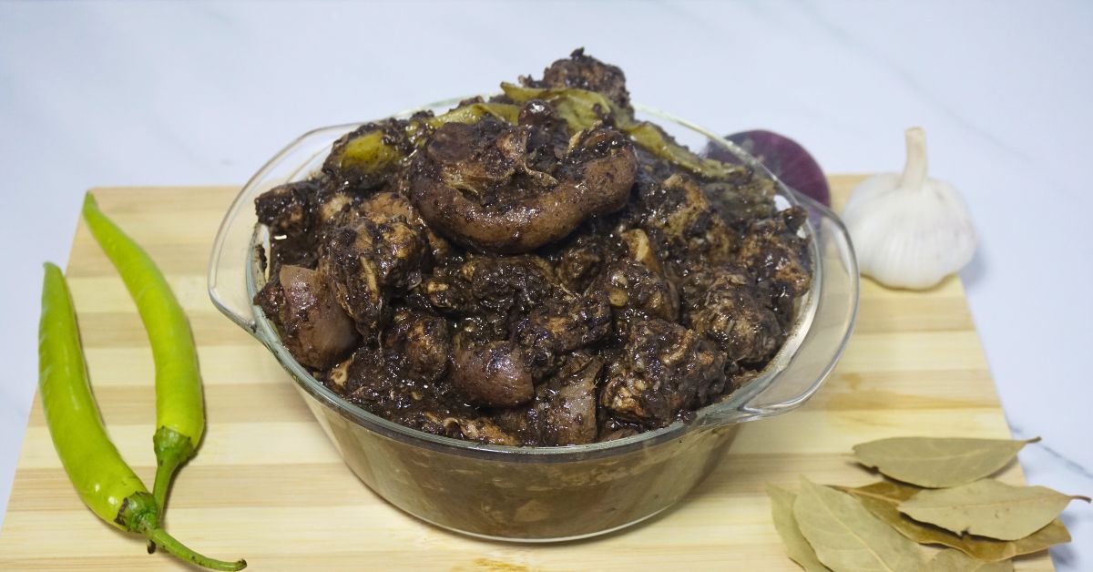 Bowl of dinuguan in a wooden chopping board with green chilies, bay leaves, onion and garlic.