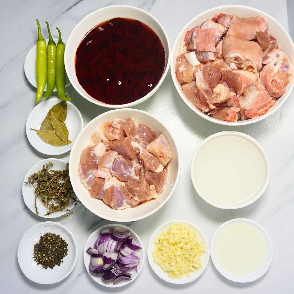Dinuguan ingredients. Pork leg, pork belly, pork blood, green chilies, bay leaves, dried oregano, black pepper, cooking oil, vinegar, garlic and onion.