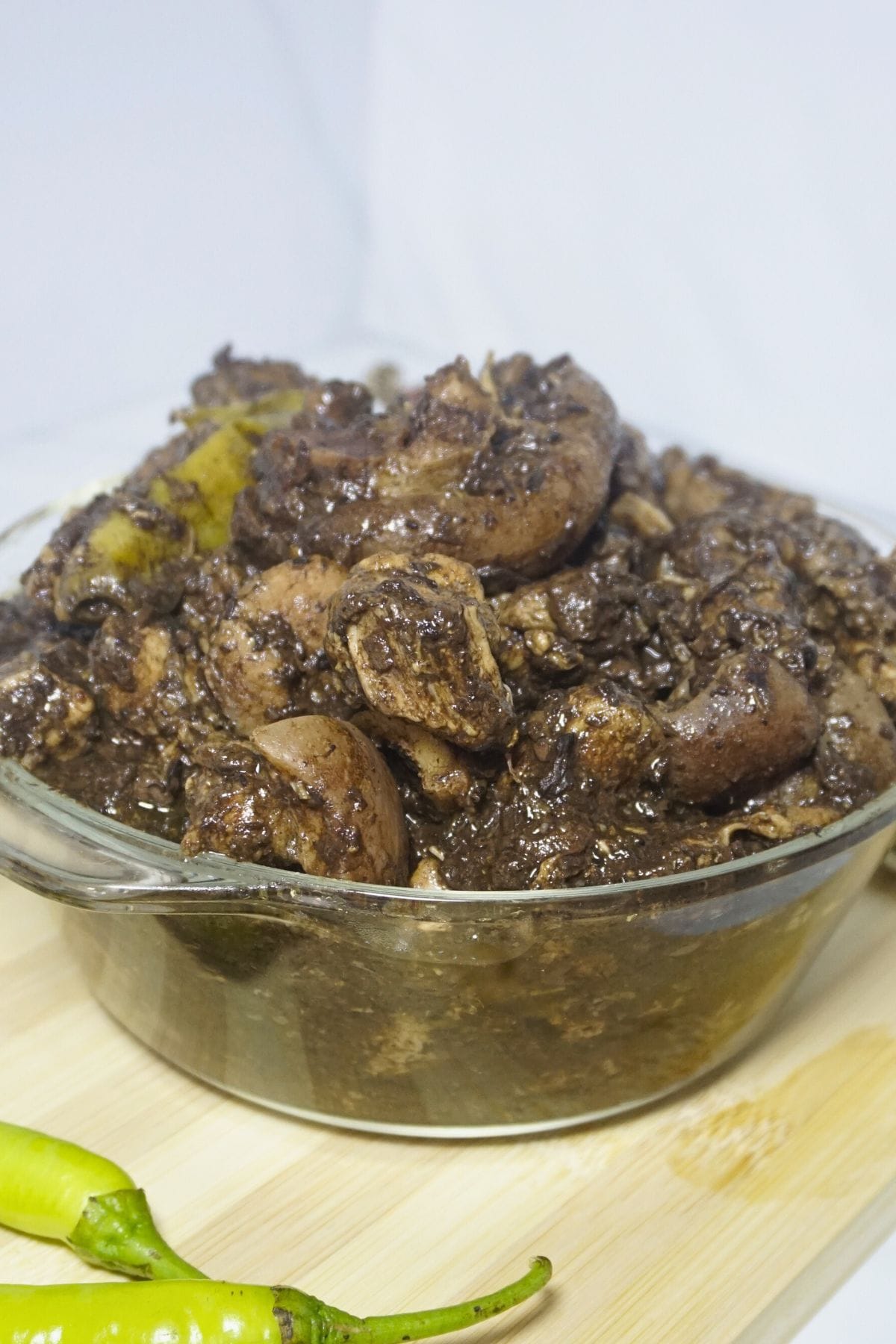 Bowl of pork dinuguan with fresh green chilies on a wooden chopping board.