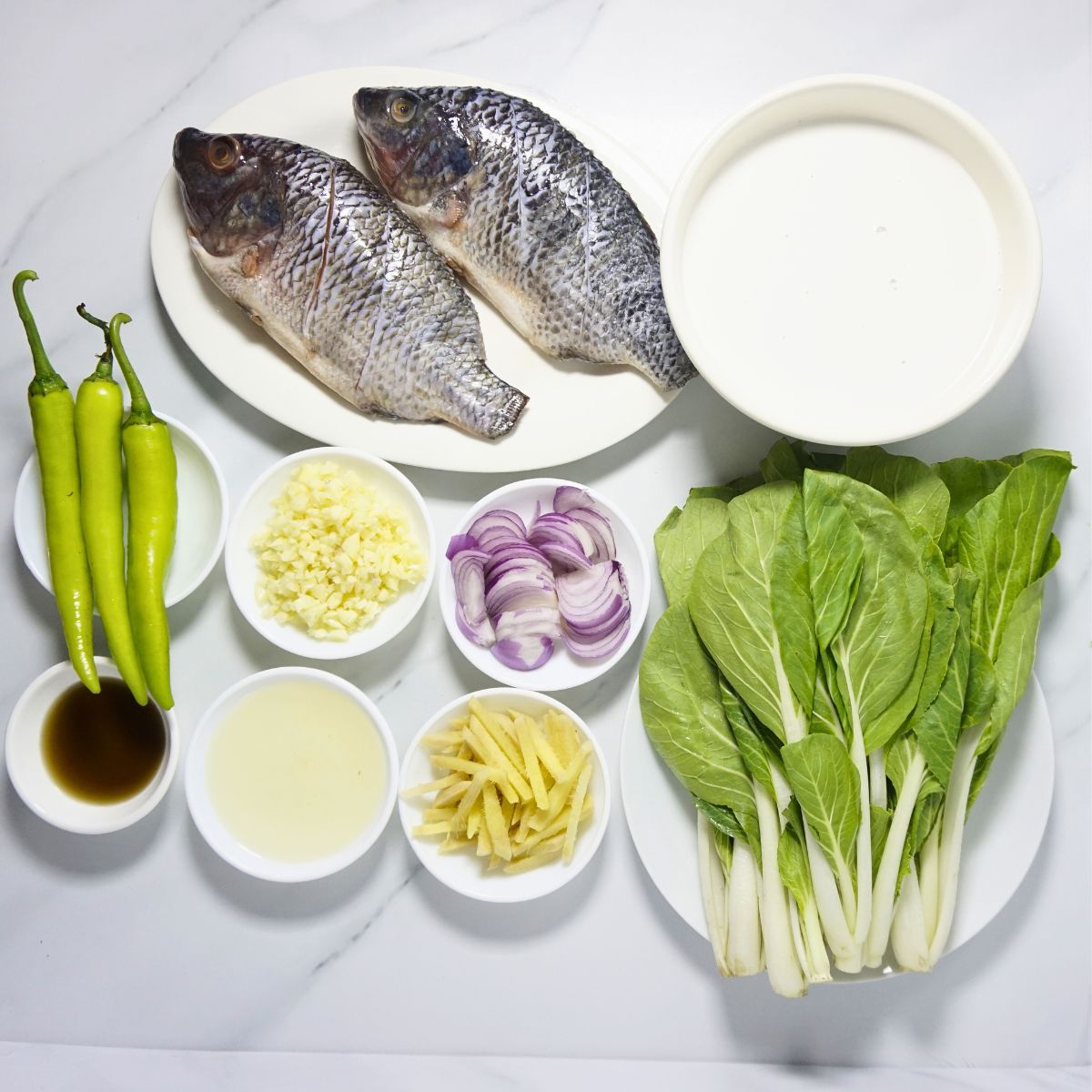 Ginataang tilapia ingredients. Tilapia, coconut cream, green chilies, pechay, cooking oil, onion, garlic, ginger and fish sauce.