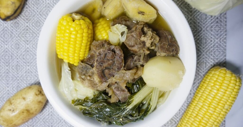 Nilagang baka with raw potatoes, sweet corn, sweet plantain and cabbage on a table.