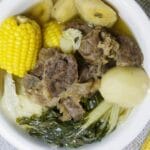 Nilagang baka with raw potatoes, sweet corn, sweet plantain and cabbage on a table.