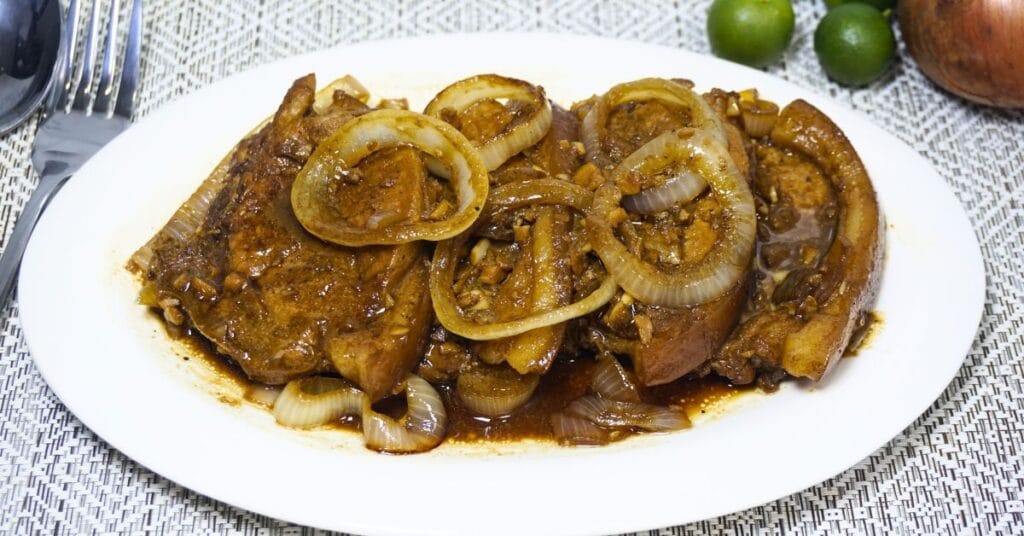 Plate of pork steak with fresh calamansi and onions on a table.