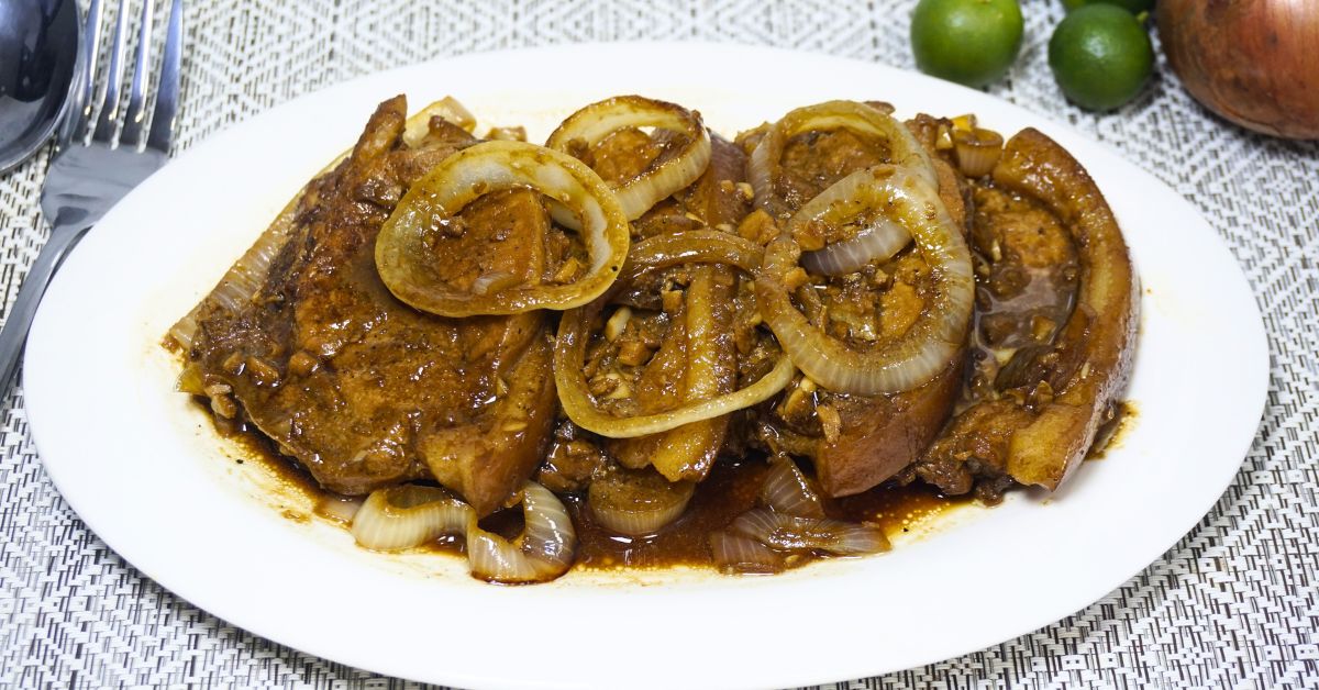 Plate of pork steak with fresh calamansi and onions on a table.