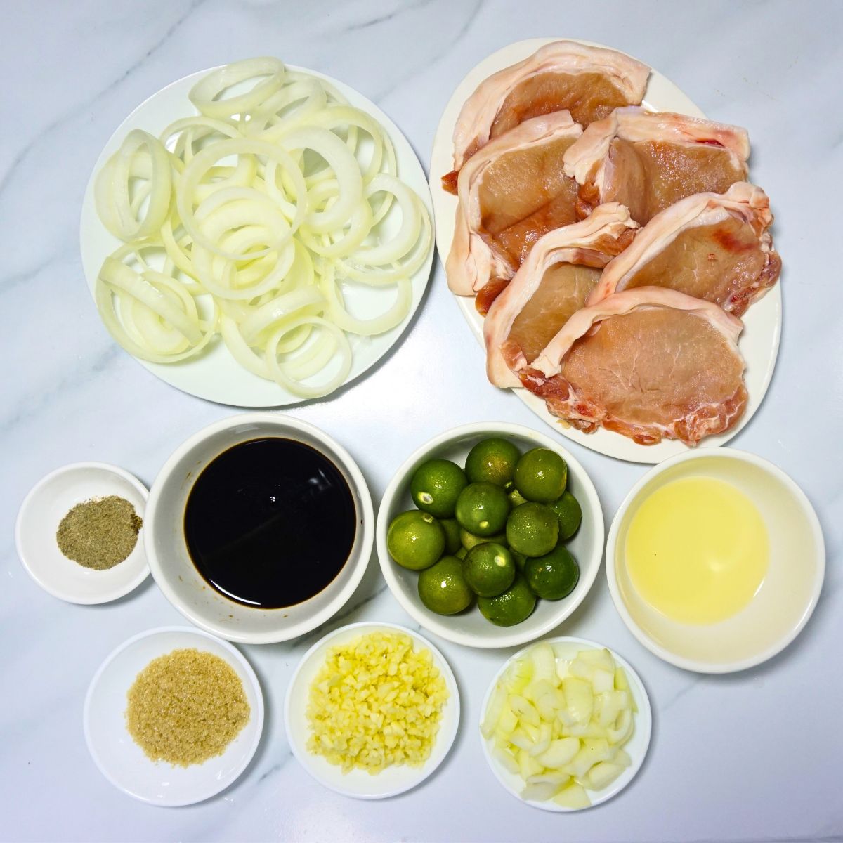 Pork steak ingredients. Pork chops, onion rings, black pepper, soy sauce, calamansi, cooking oil, fish sauce, garlic and onion.