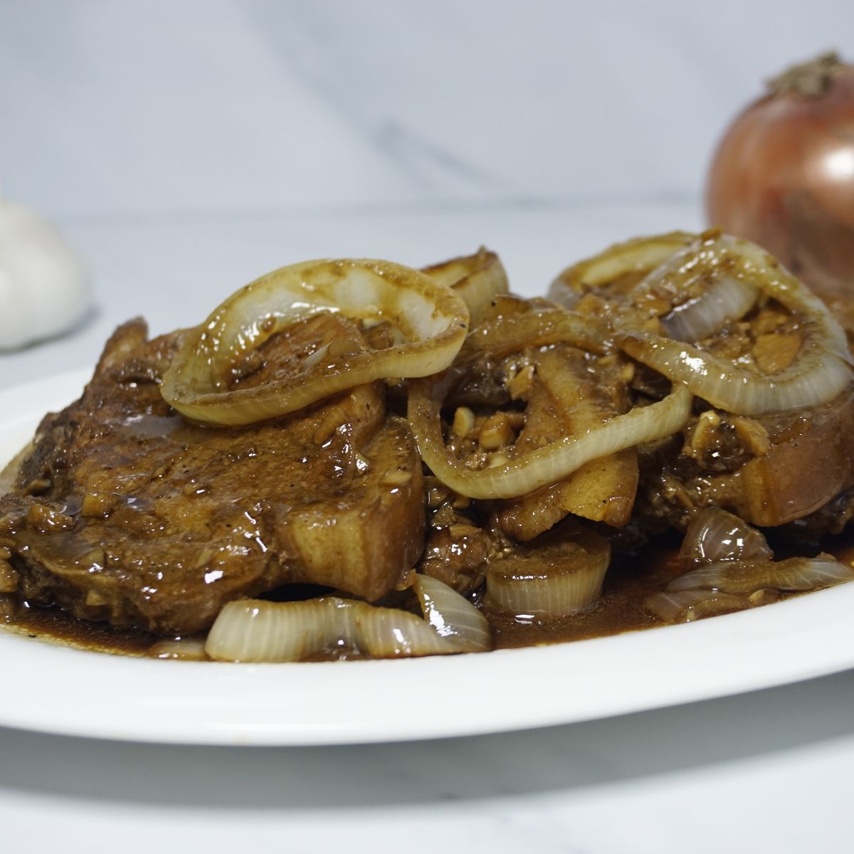 Slices of pork chops in soy sauce with onion rings on top.