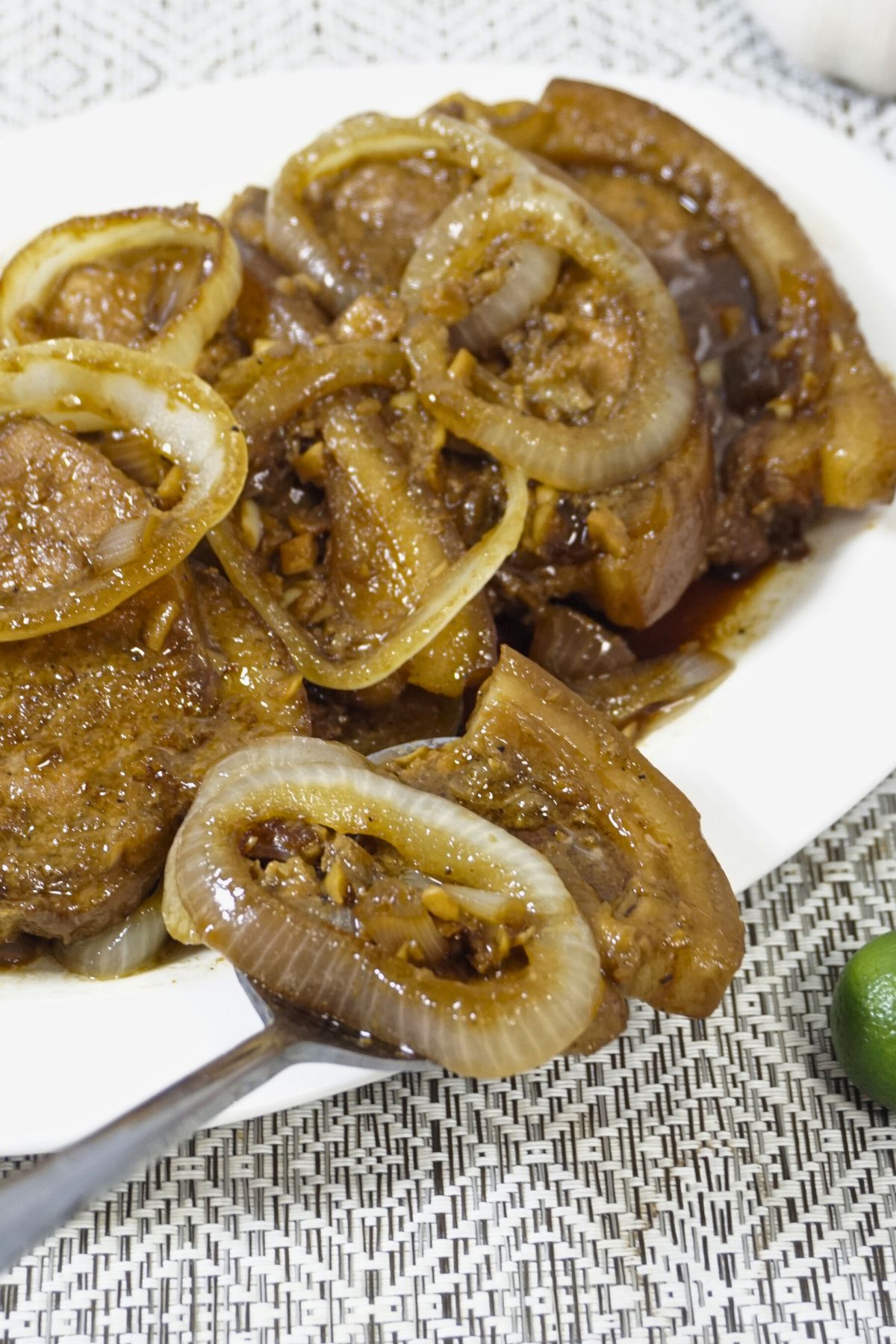 Spoon scooping a slice of pork steak with onion rings.