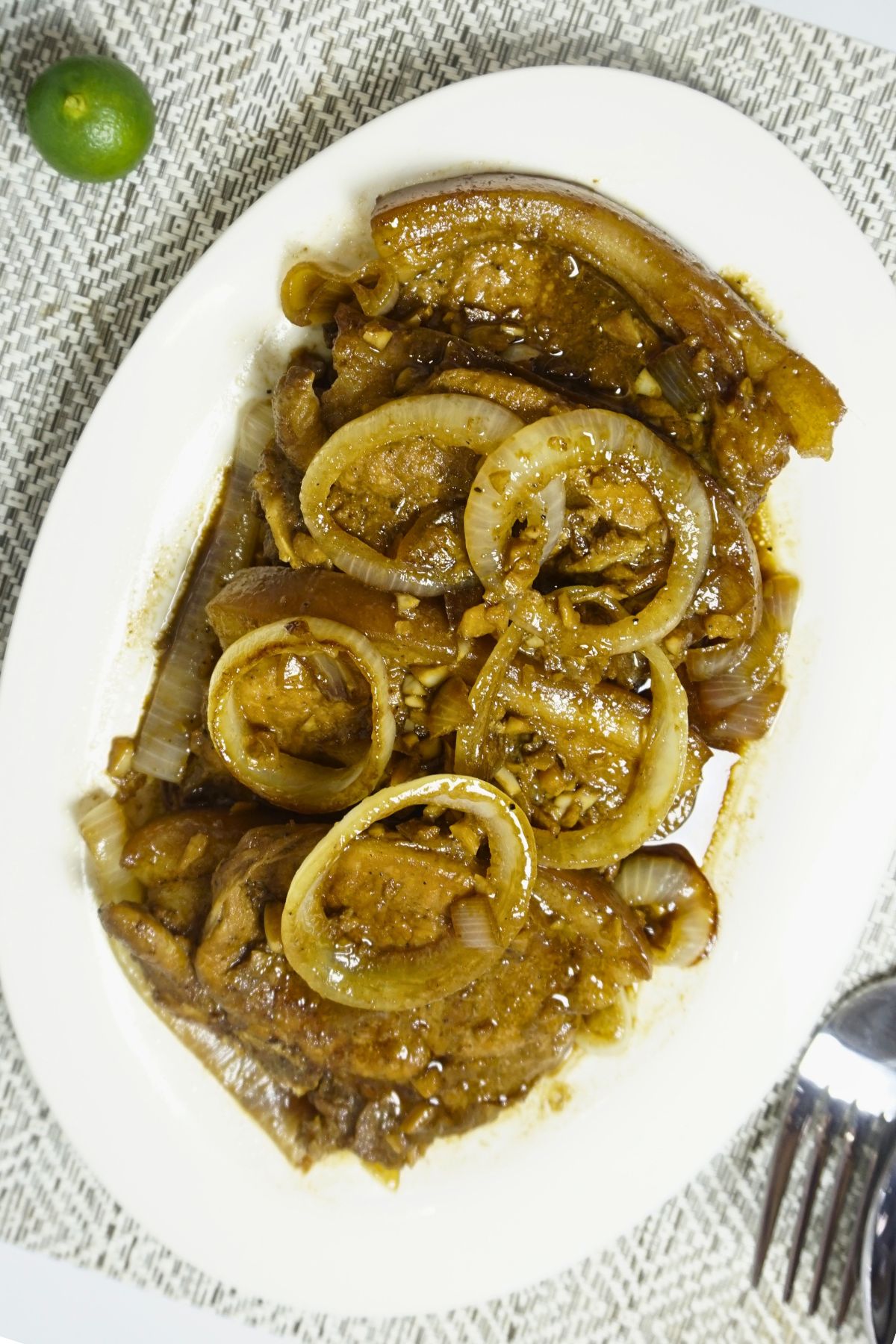 Pork chops cooked in calamansi juice and soy sauce with onion rings on top.