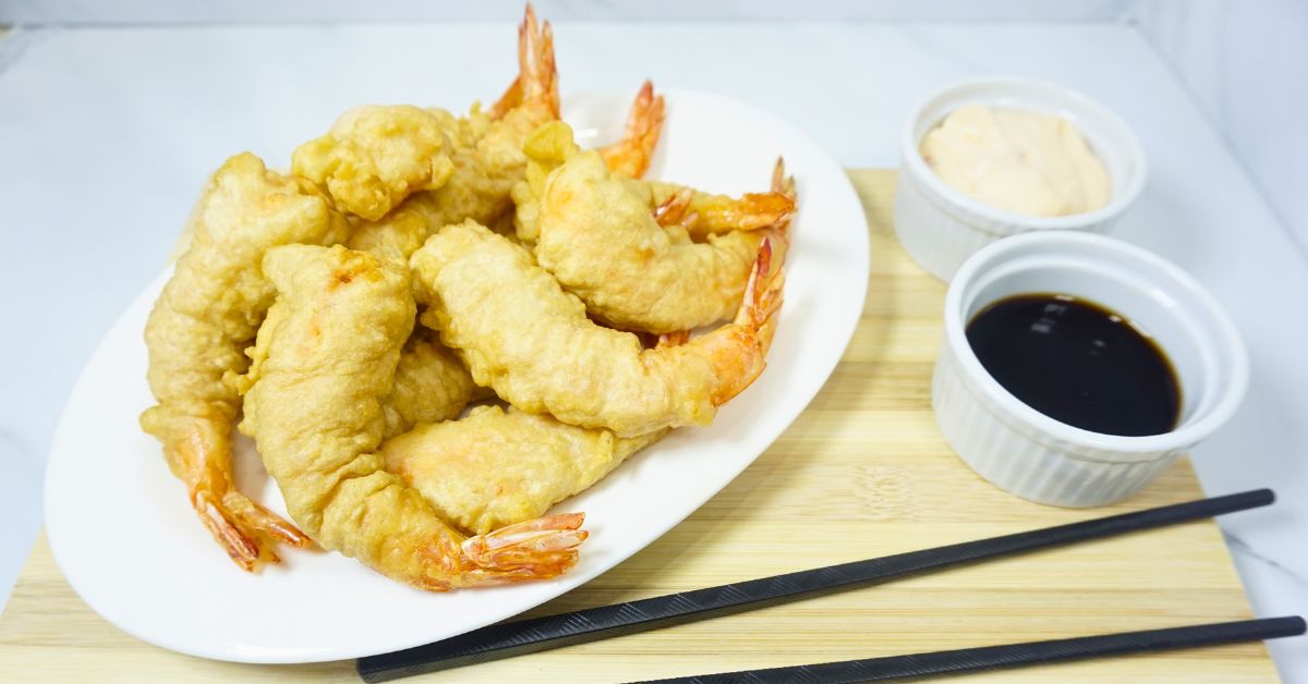 Plate of shrimp tempura with dipping sauce on a wooden board.