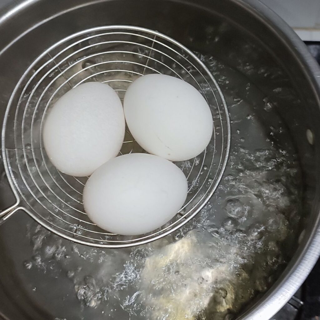 Raw eggs in a strainer on top of a pot with boiling water.