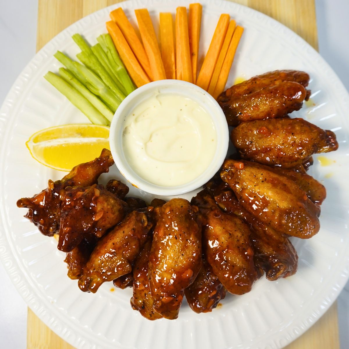 Plate of buffalo wings with celery sticks, carrot sticks, lemon slice and blue cheese dressing.