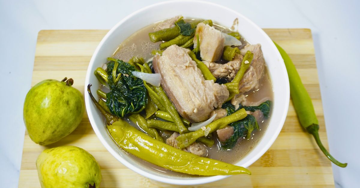 Bowl of pork bulanglang with fresh guavas and green chili in a wooden cutting board.