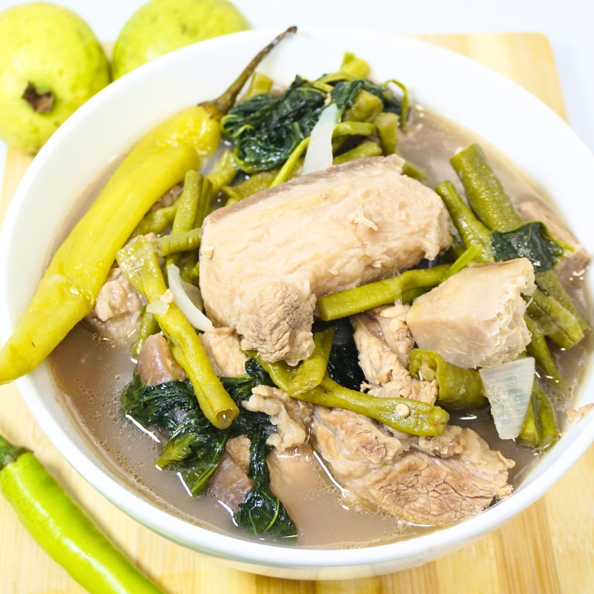 Bowl of bulanglang baboy in a wooden board with green chili and guavas.