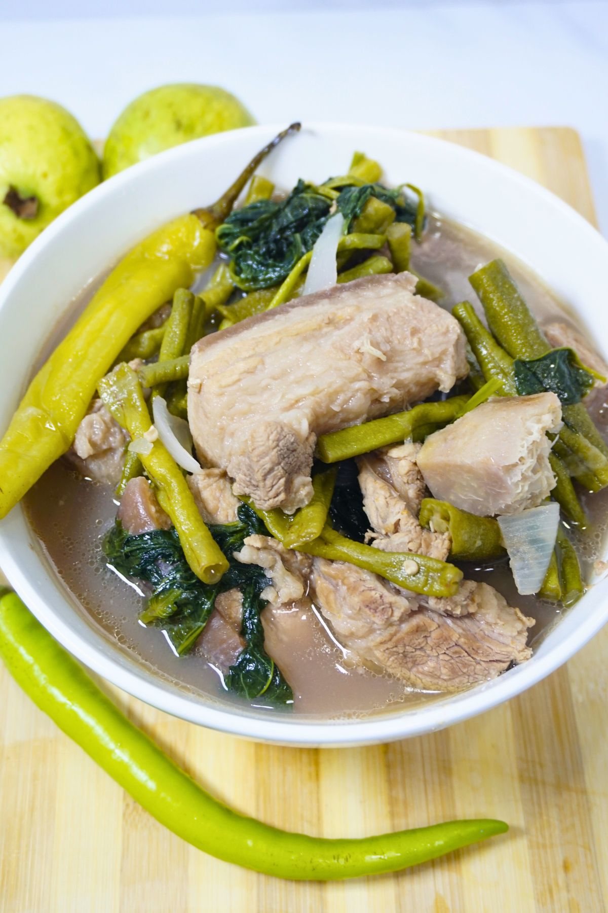 Sinigang na baboy sa bayabas in a bowl with fresh guavas and green chili.