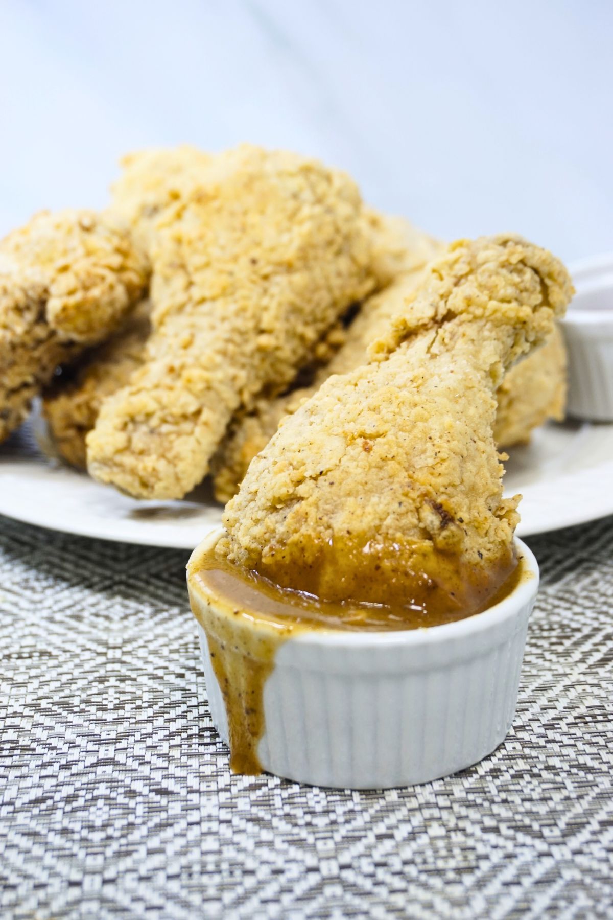 Crispy fried chicken leg deep in ramekin dish with gravy.