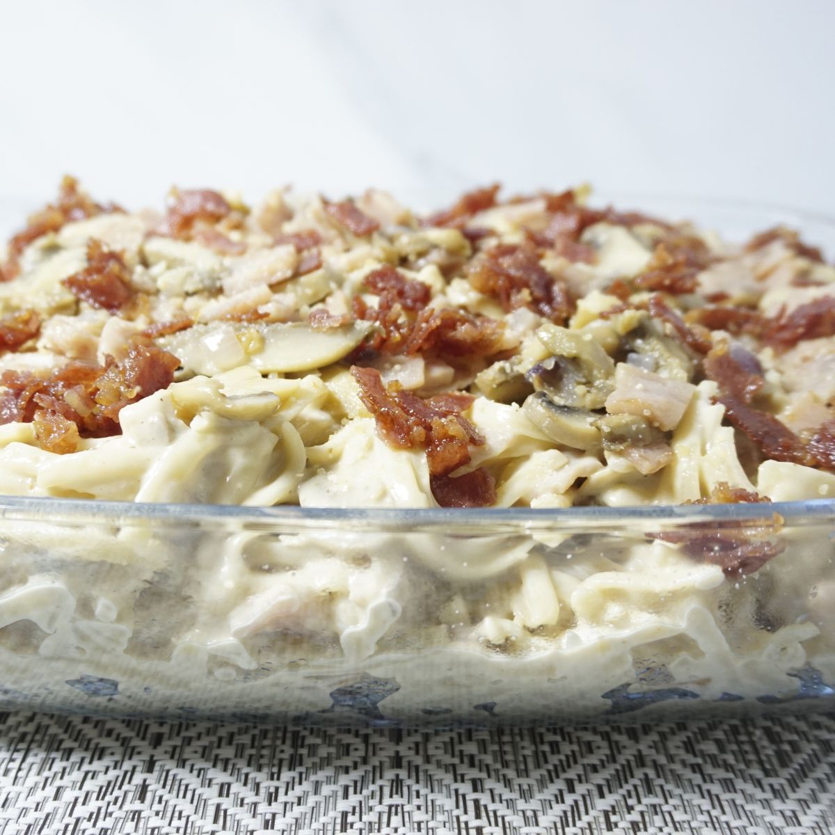 Pasta in a baking dish top with white sauce and bacon bits.