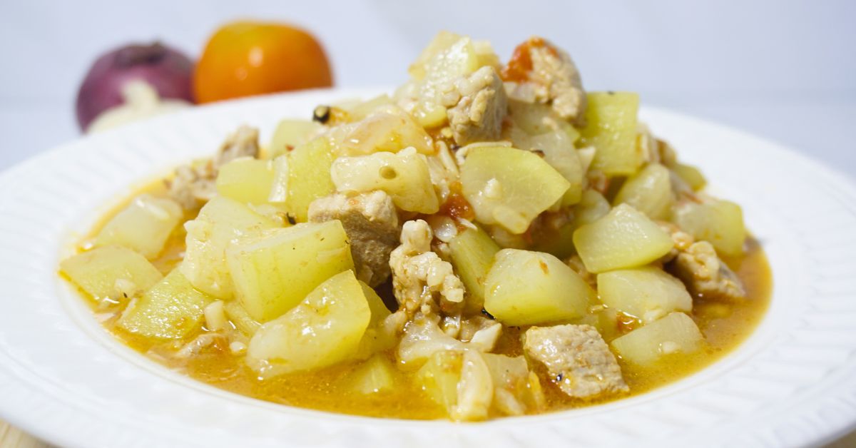 Ginisang upo in a plate with fresh onion and tomato in the background.