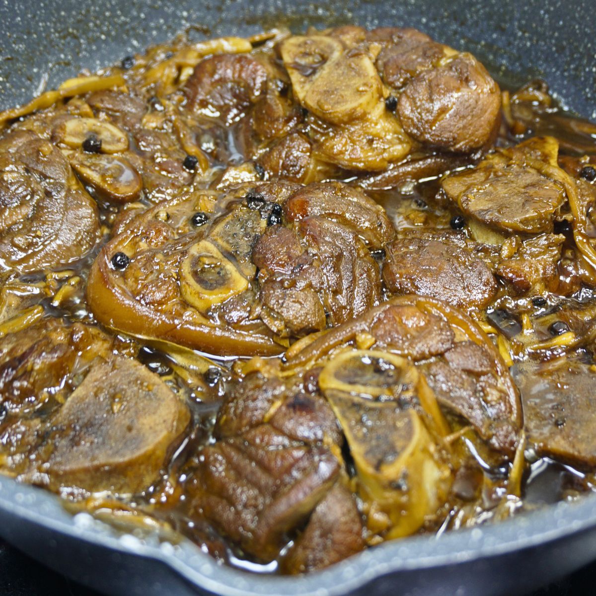 Paksiw na pata in a pan with banana blossom and peppercorns.