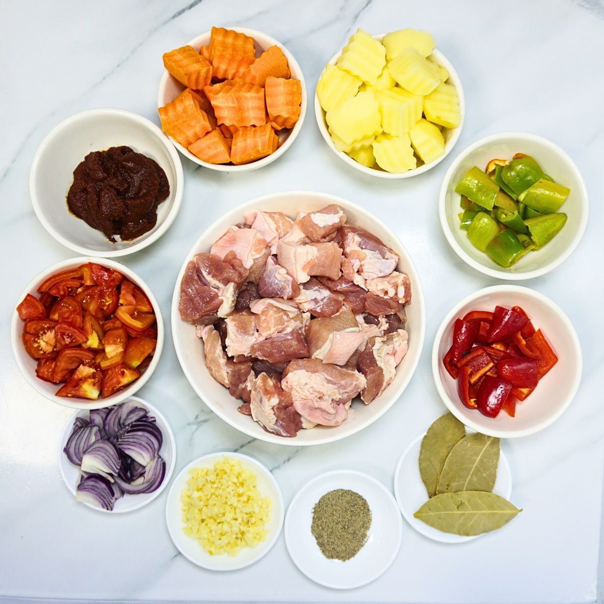 Pork afritada ingredients. Pork belly, garlic, onion, tomatoes, tomato paste, carrots, potatoes, bell peppers, black pepper powder and dried bay leaves.