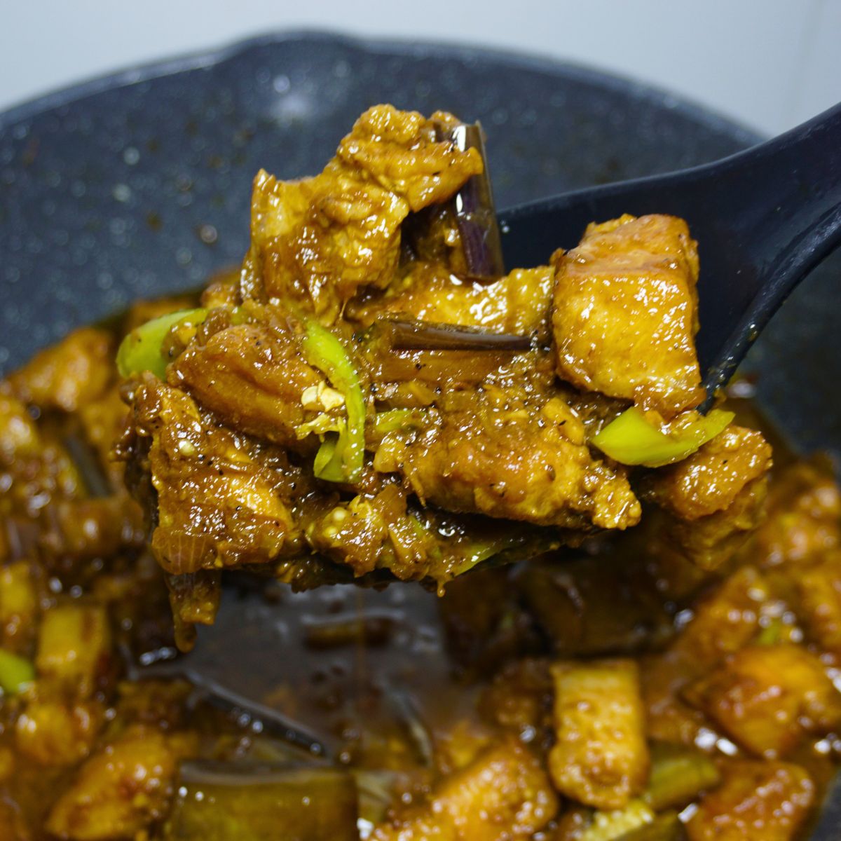 Ladle scooping a portion of pork binagoongan in a pan.