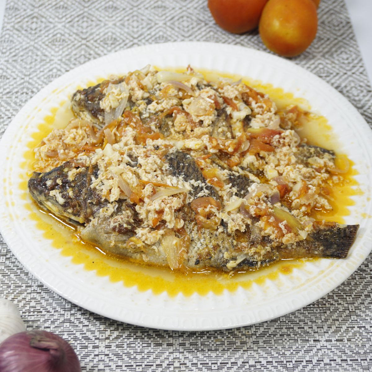 Plate of sarciadong tilapia with fresh tomatoes, garlic and onion on a table.