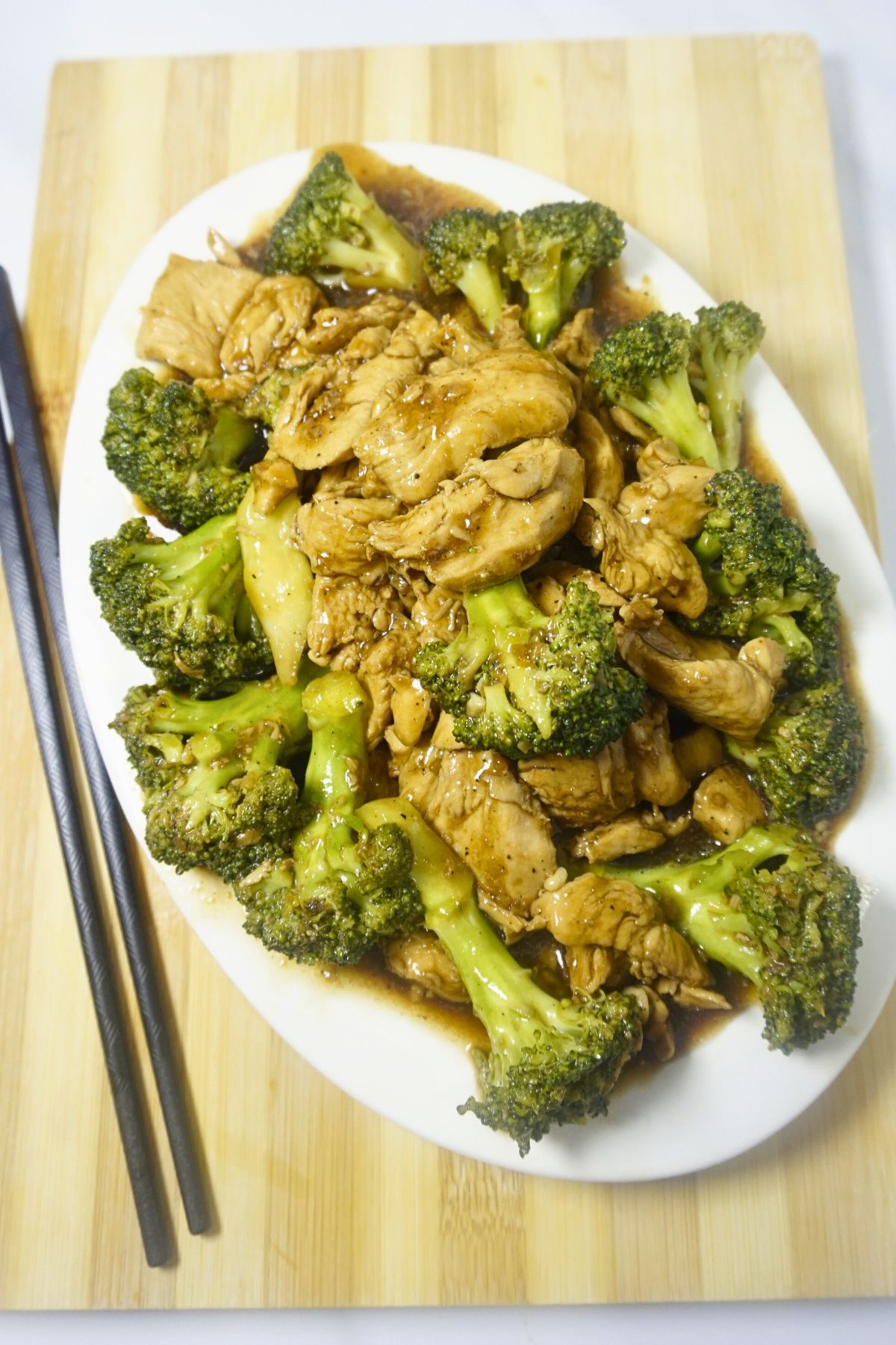 Plate of chicken broccoli with chopsticks on a wooden cutting board.