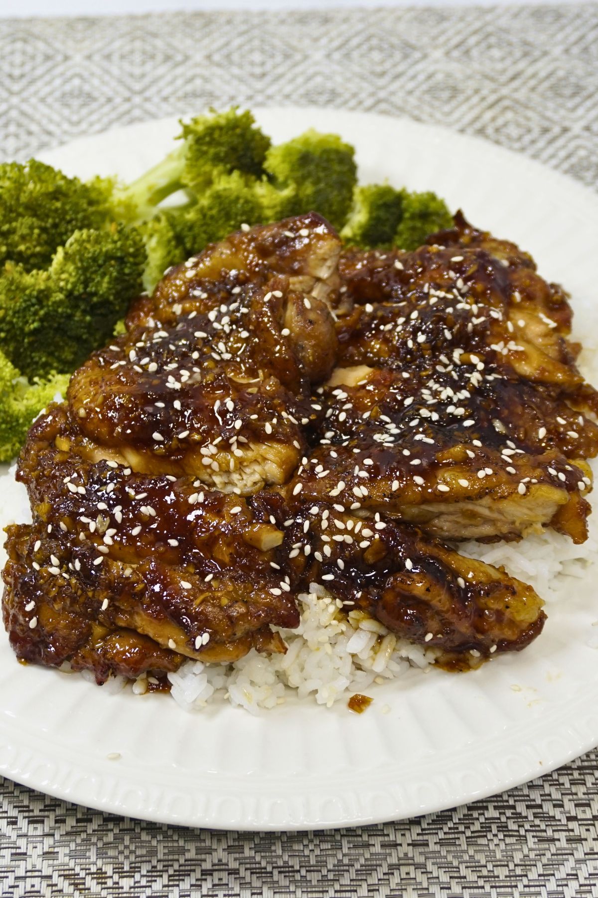 Chicken teriyaki on top of a white rice garnished with broccoli.