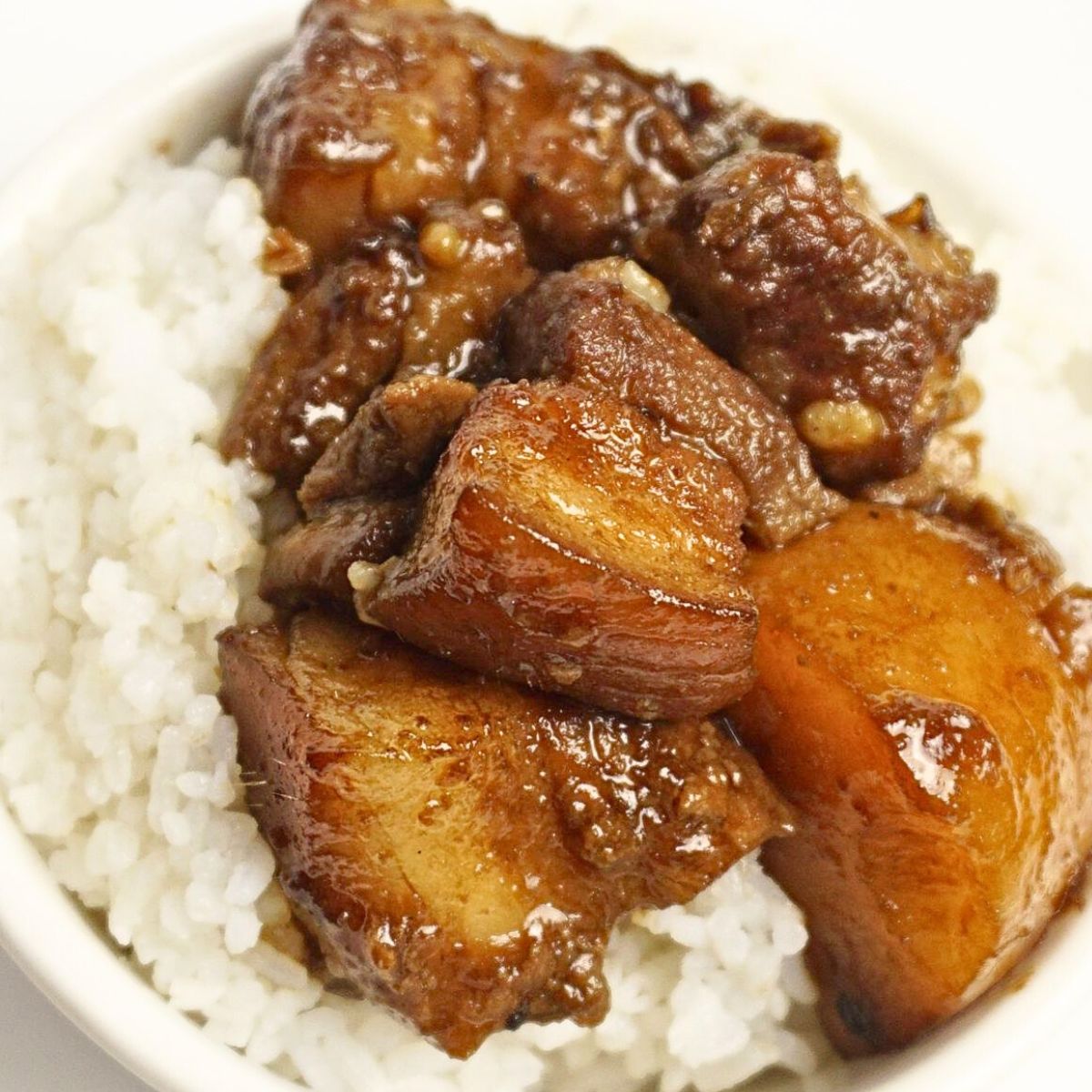 Pork adobo served on top of rice in a white bowl.