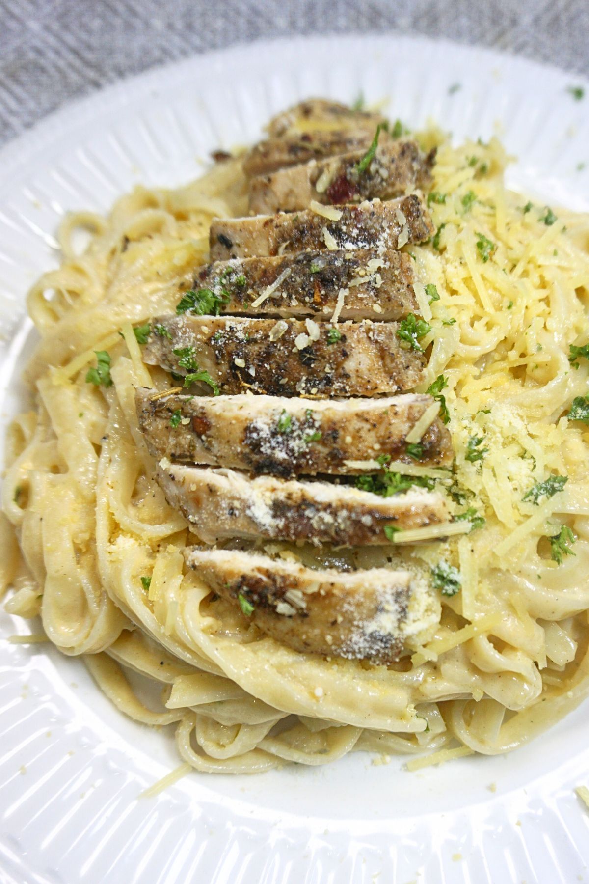 A serving of creamy chicken alfredo with sliced chicken on top sprinkled with cheese and parsley.