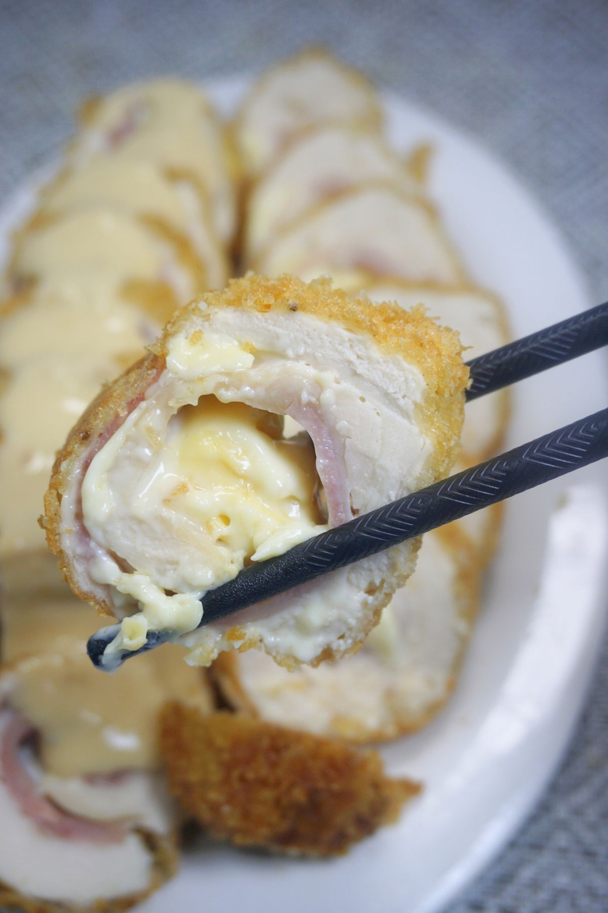 A pair of wooden chopsticks holding a slice of chicken cordon bleu.